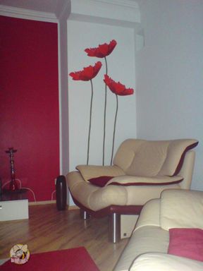 Wohnzimmer in der eine Wandabteil in dunkelrot mit Pinkanteil gestrichen wurde, de restlichen Wand weiß und ein schmales Stück Wand wurde mit 3 riesigen Mohnblumen, die vom Boden bis zur Decke reichen, in der Farbe der roten Wand verziert.