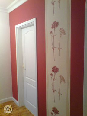 farbliche Innenraum Gestaltung mit einer Wand in rot und vertikaler Bordüre in Sandfarben und roten Neckende sich auf die Länge wiederholen. eine weiße Holzkassettentür ist zu sehen.